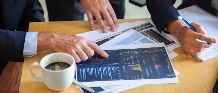 Unrecognizable businessman pointing at printed chart and showing graph to colleagues. Professional content partners making notes for statistics. Cooperation, communication and partnership concept